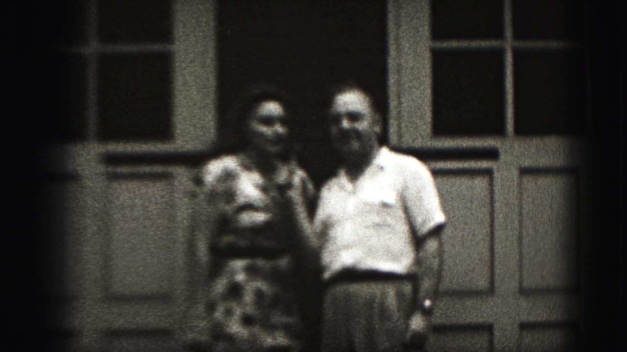 Adult couple standing close together in front of paneled doors.