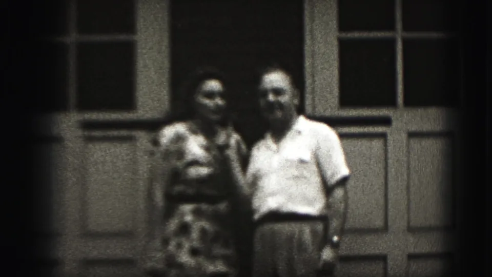 In supported 1946 New Cumberland home-movie footage, an adult couple stands close together outside paneled doors.