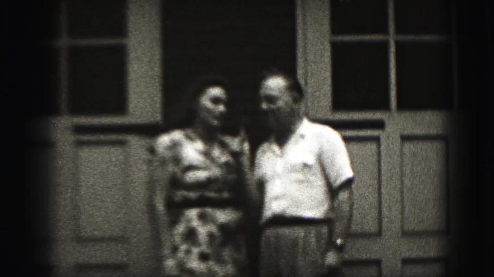 In 1946 New Cumberland home-movie footage, an adult couple stands close outside a paneled door and tall window.