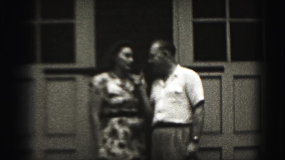 In this 1946 New Cumberland home-movie frame, an adult couple stands close on a porch beside a multi-pane window and door.