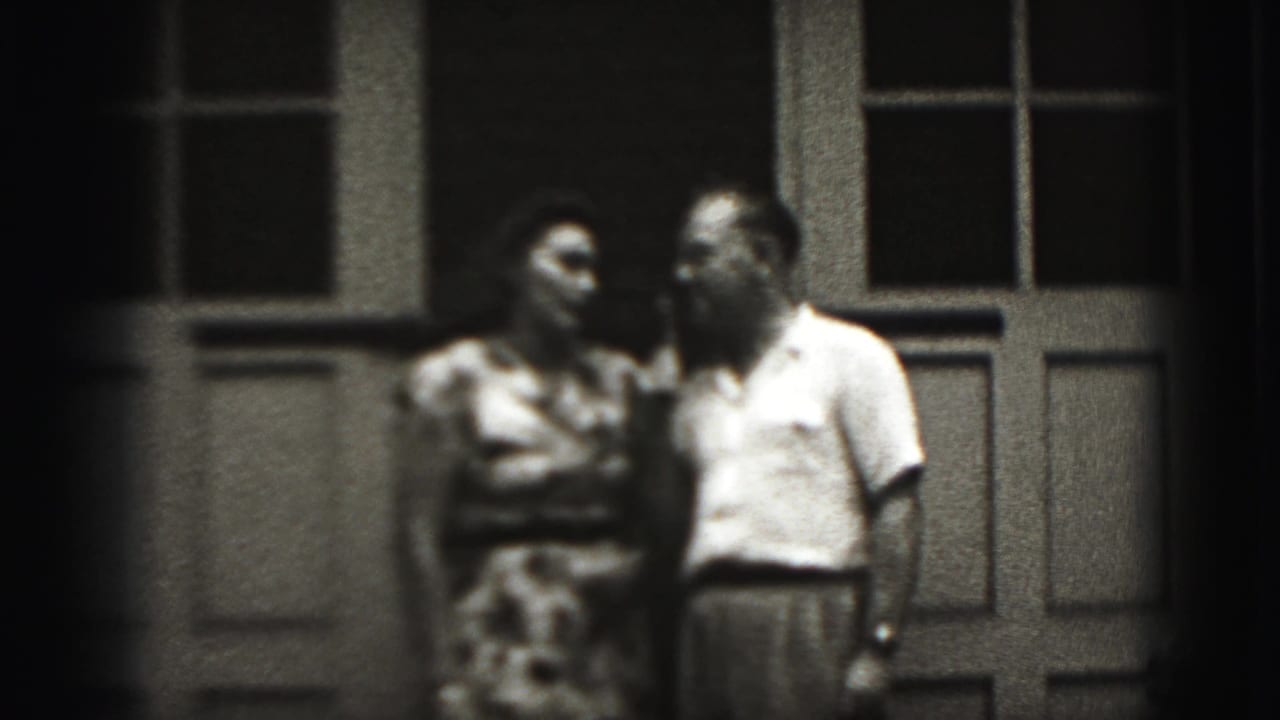 Adult couple facing each other near a porch window and doorway.