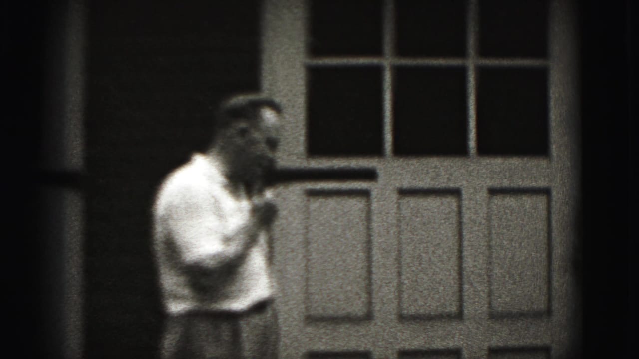 Adult man turns partly sideways at a New Cumberland doorway, still holding a small object near his mouth in the 1946 footage.