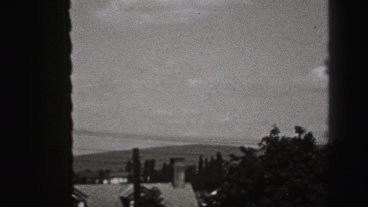 A 1946 home-movie window view shows rooftops, trees, and distant hills beyond the house.