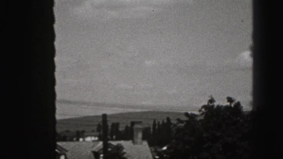 A 1946 home-movie window view shows rooftops, trees, and distant hills beyond the house.