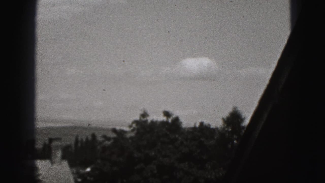 Black-and-white 8mm view in New Cumberland, Pennsylvania, showing rooftops, trees, sky, and distant hills through dark framing.