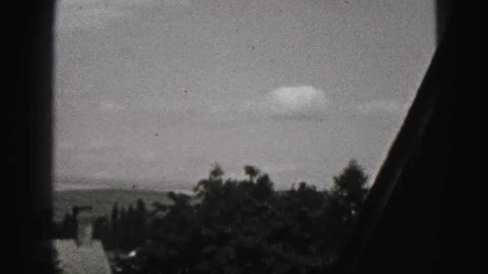 Black-and-white 8mm view in New Cumberland, Pennsylvania, showing rooftops, trees, sky, and distant hills through dark framing.