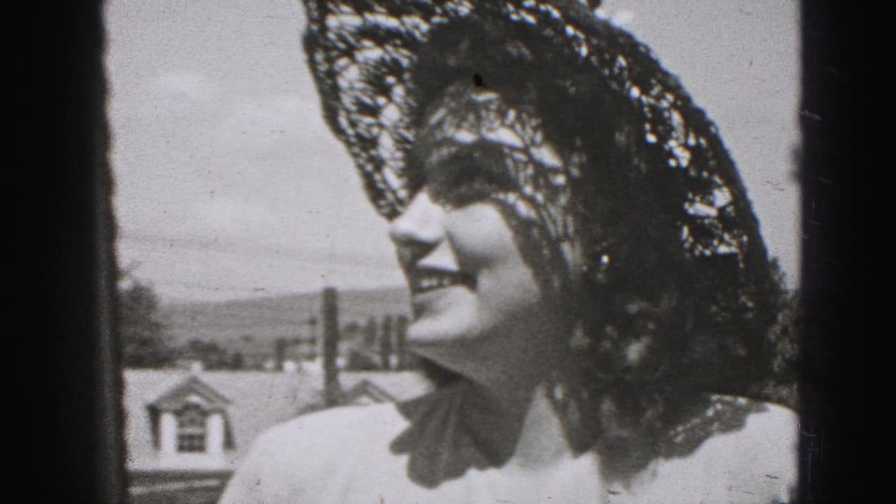 In 1946 New Cumberland footage, a smiling adult woman in a lace hat is framed near rooftops, sky, and a dark vertical edge.
