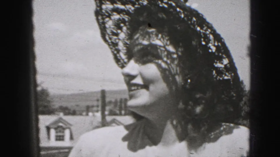 In 1946 New Cumberland footage, a smiling adult woman in a lace hat is framed near rooftops, sky, and a dark vertical edge.
