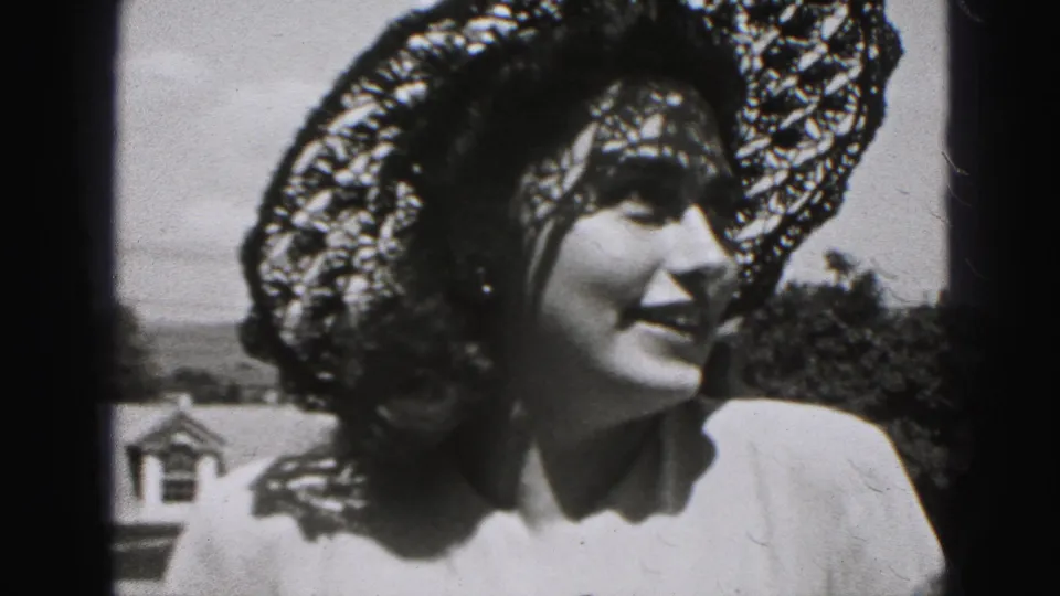 Smiling woman in a broad patterned lace hat stands outdoors in 1946 New Cumberland home-movie footage.
