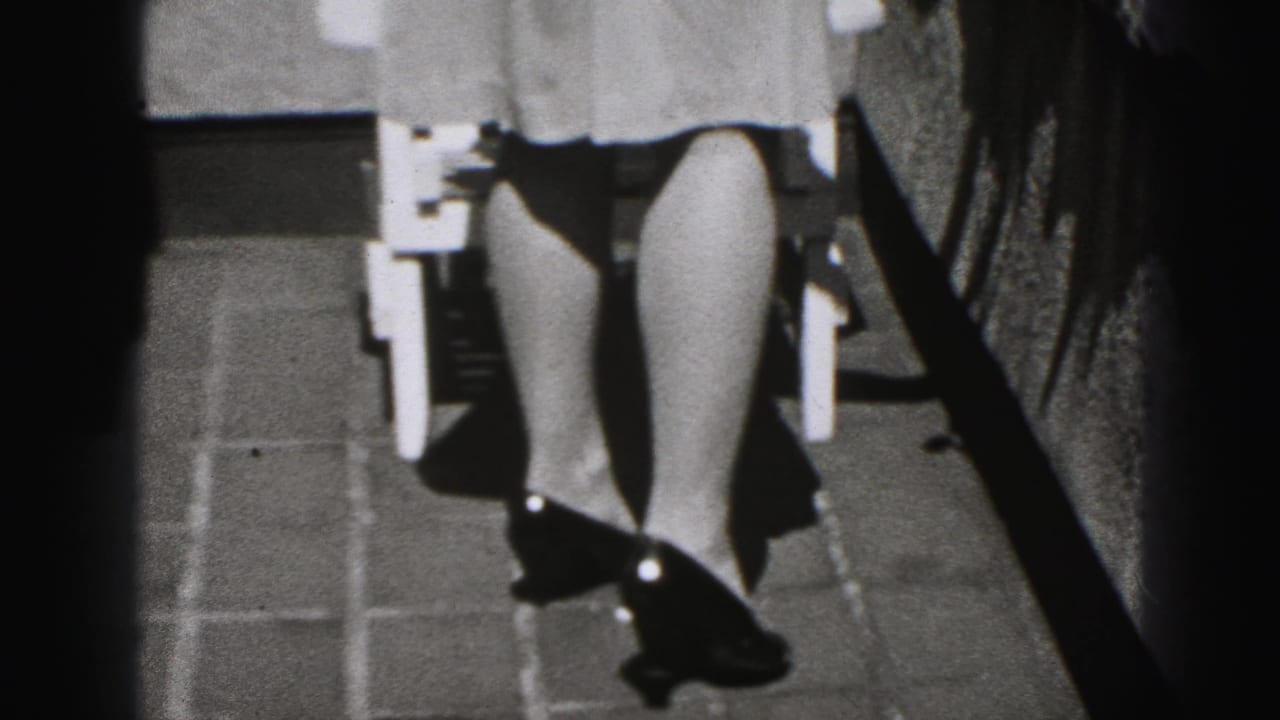 Lower view of a woman’s dress, legs, and high heels near an outdoor chair.