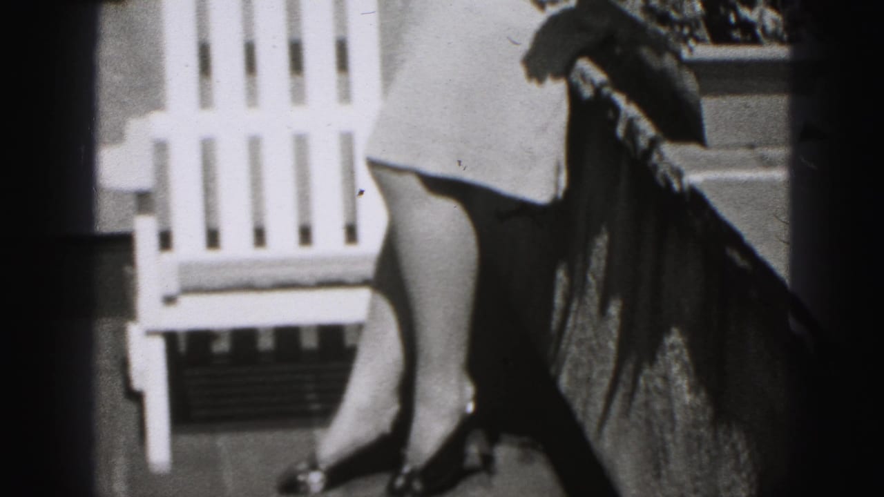 Woman's legs beside a white outdoor chair on a balcony, with dark film edge shadows.