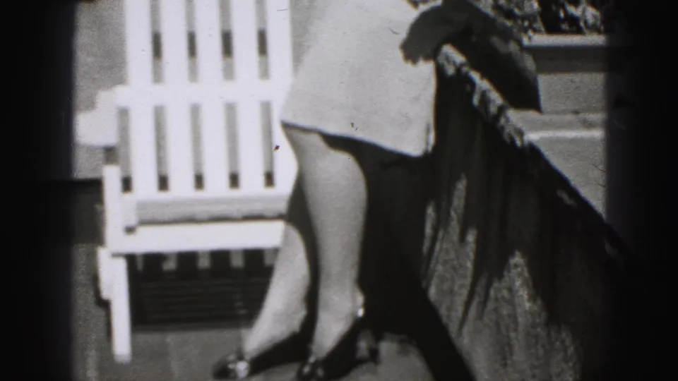 1946 New Cumberland home-movie frame showing a woman partly cropped beside a white balcony chair and railing.