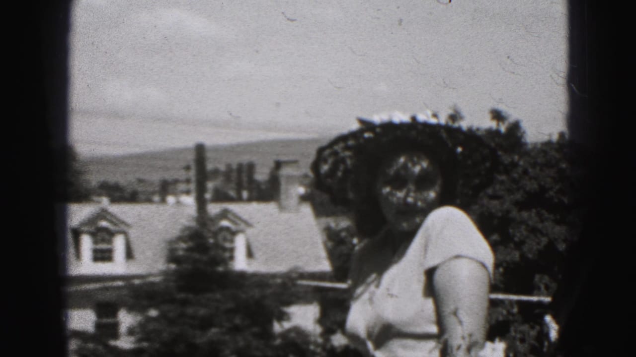 Woman in a wide-brimmed hat and light dress standing outdoors near houses and trees.