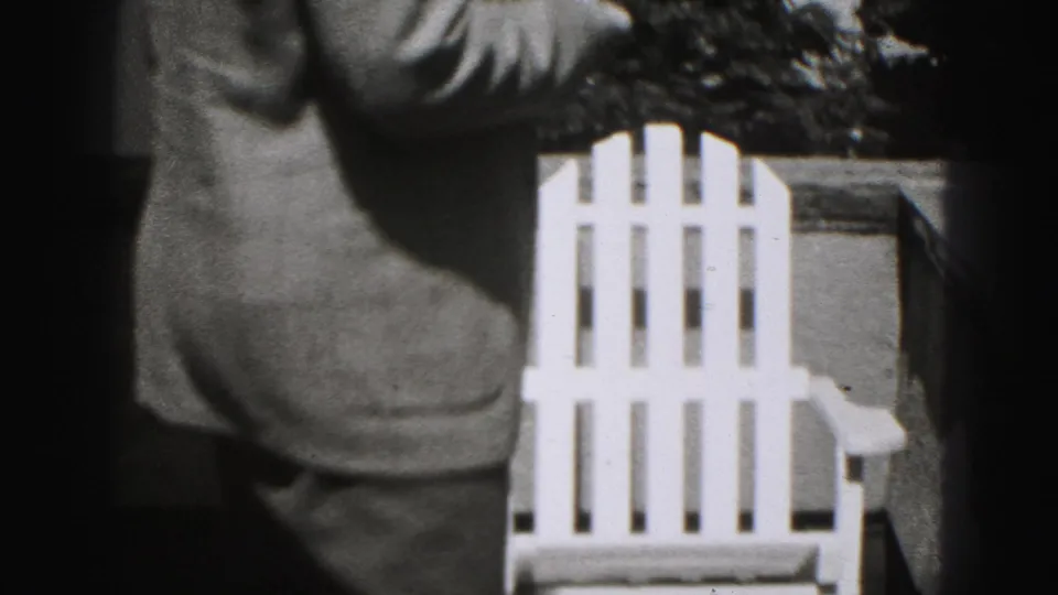 The suited man turns from the camera near a white Adirondack-style chair in the outdoor 1946 New Cumberland scene.