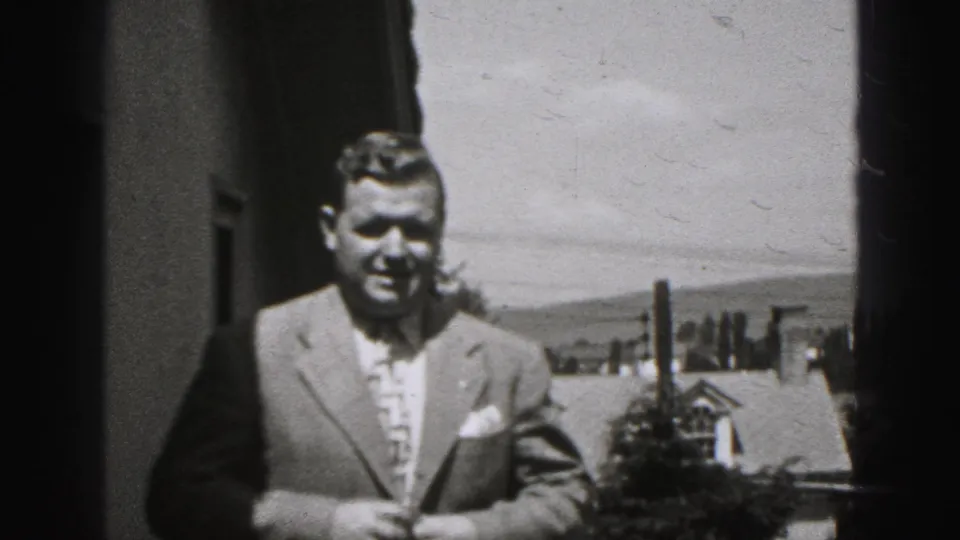 In 1946 New Cumberland, Pennsylvania footage, a middle-aged man in a suit faces the camera outside near a house and trees.