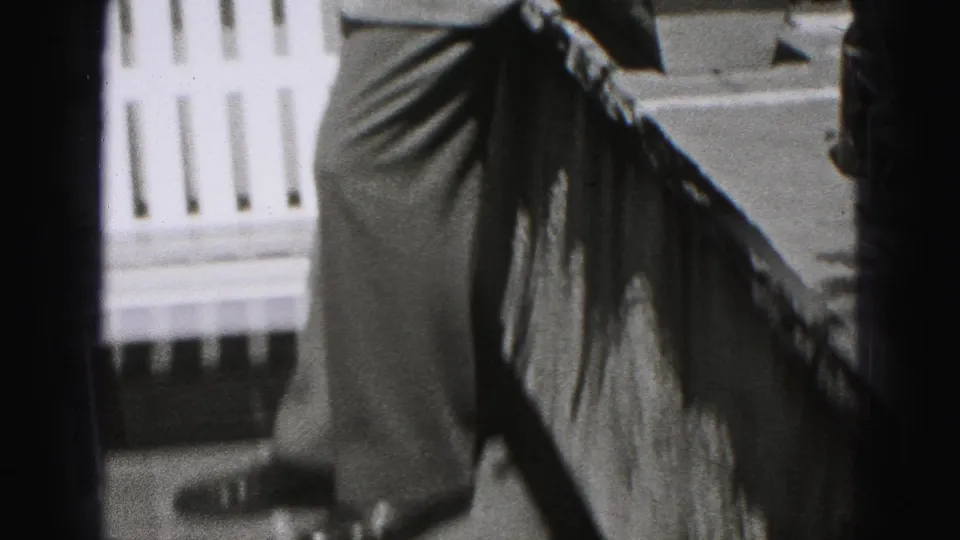 A suited adult man stands near a railing in New Cumberland, Pennsylvania, with a white picket fence and residential architecture behind him.