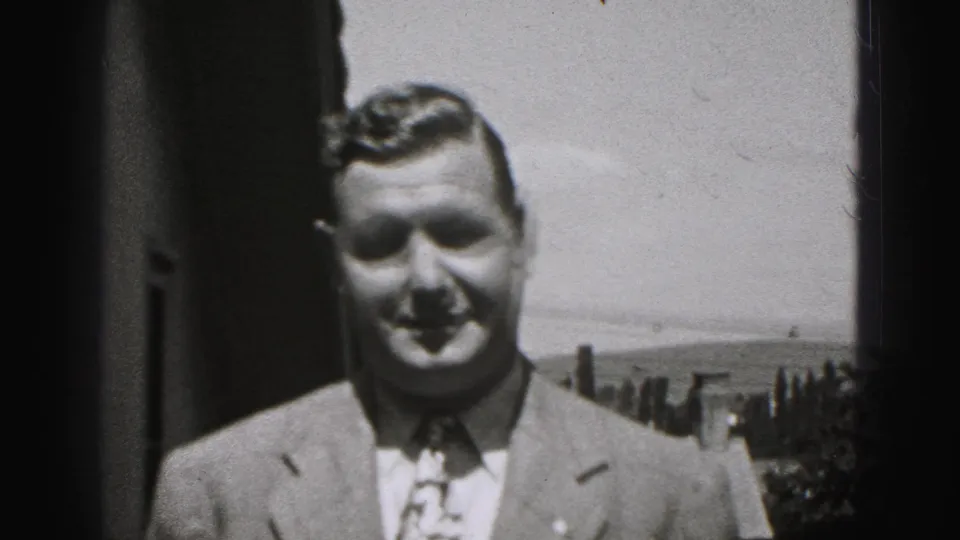 Man in a suit and patterned tie faces the camera outdoors in the supplied 1946 New Cumberland home-movie setting.