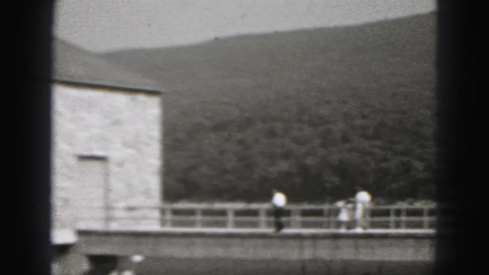 A 1946 New Cumberland riverfront view shows walkers on a bridge near a stone pump house with wooded hills behind it.