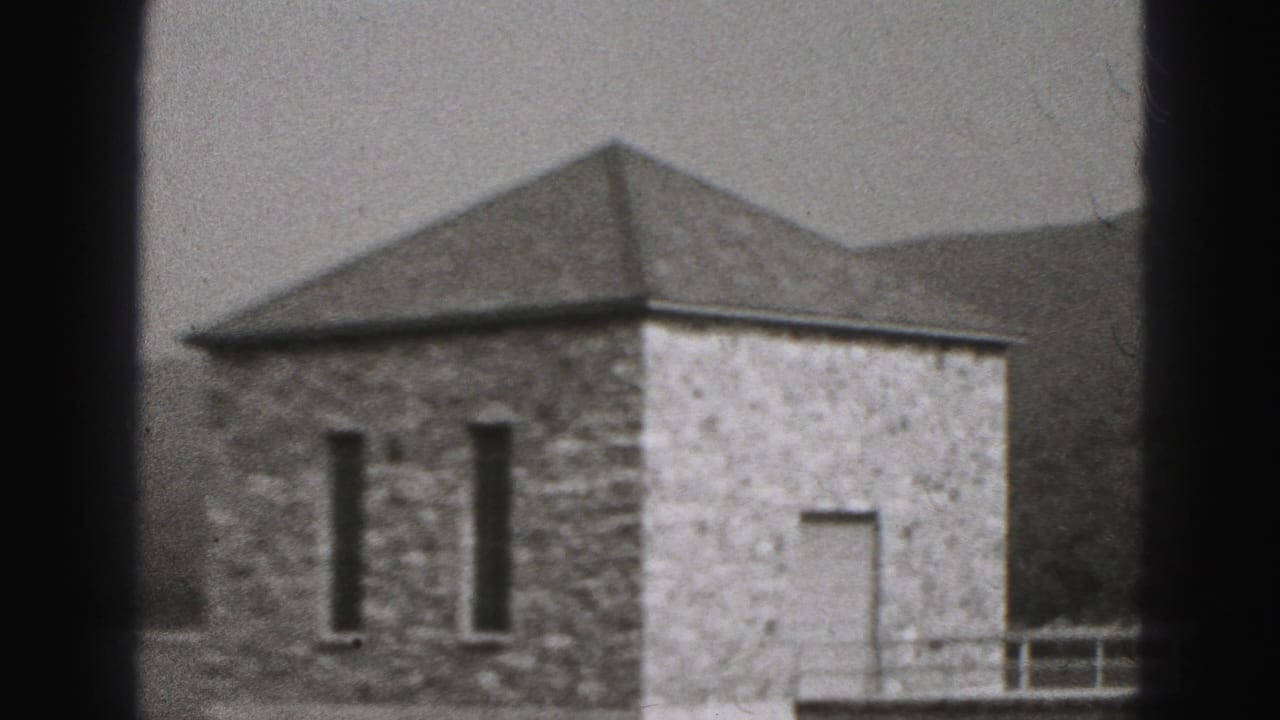 The camera settles on a stone pump house in New Cumberland, with narrow windows, a light wall section, railings, trees, and hills.