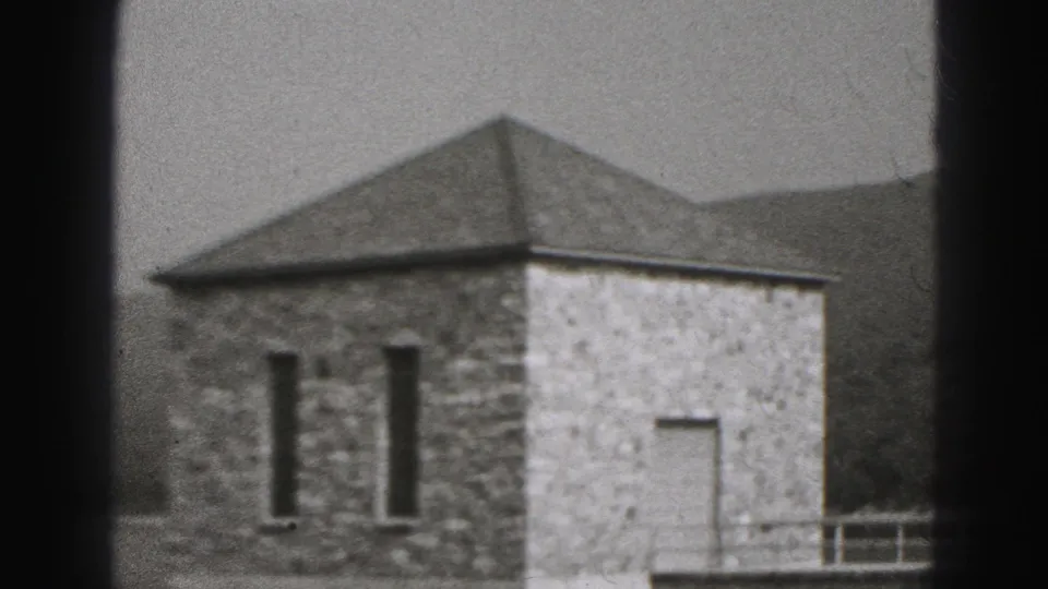 The camera settles on a stone pump house in New Cumberland, with narrow windows, a light wall section, railings, trees, and hills.