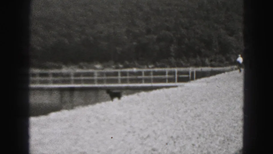 Gravel riverbank and railing with a distant person walking through the 1946 New Cumberland scene.