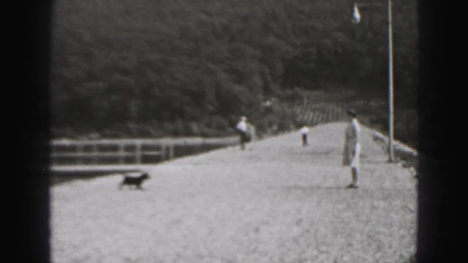 1946 New Cumberland frame with a dog on the gravel levee path, a woman near a light pole, and pedestrians farther back.