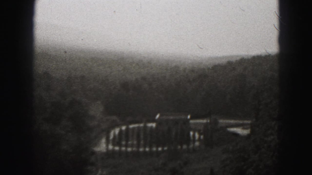 Final 1946 New Cumberland frame looking past a railing toward wooded hills under a pale sky in soft black-and-white 8mm texture.