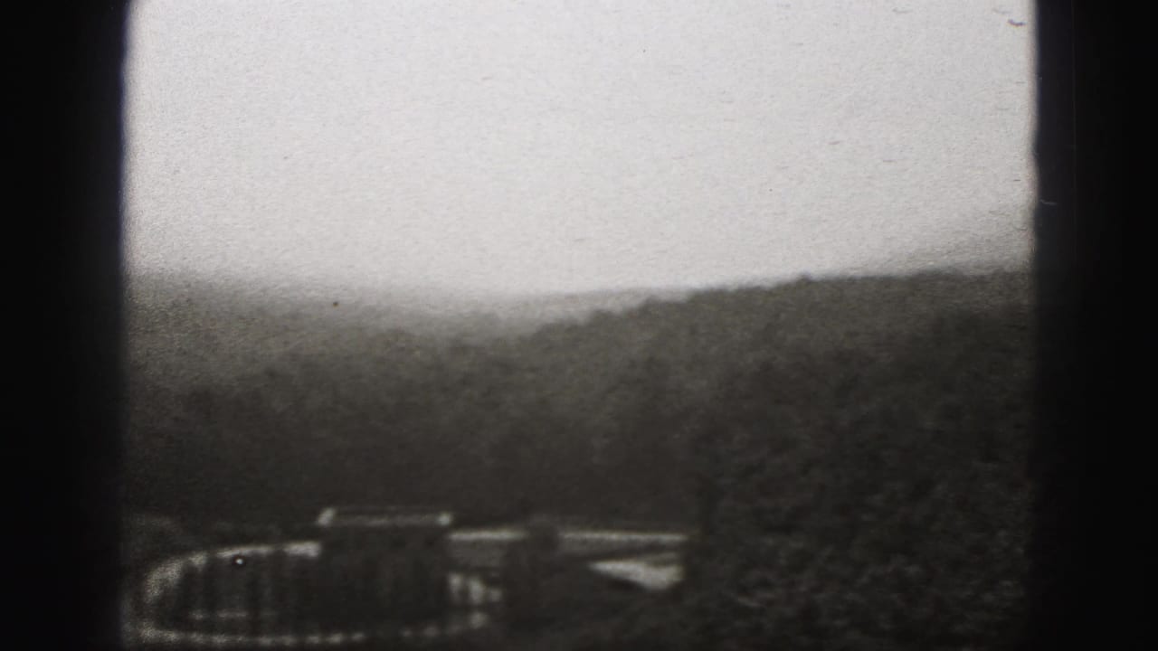 Black-and-white 8mm view over New Cumberland hills, with a small distant structure partly obscured by trees and film-edge shadows.