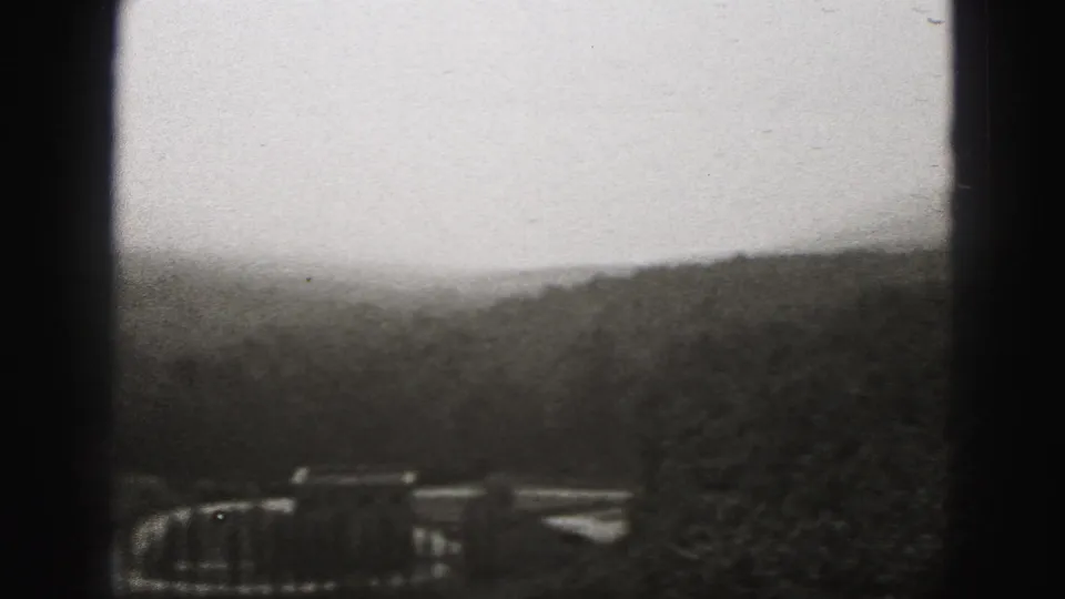 Black-and-white 8mm view over New Cumberland hills, with a small distant structure partly obscured by trees and film-edge shadows.