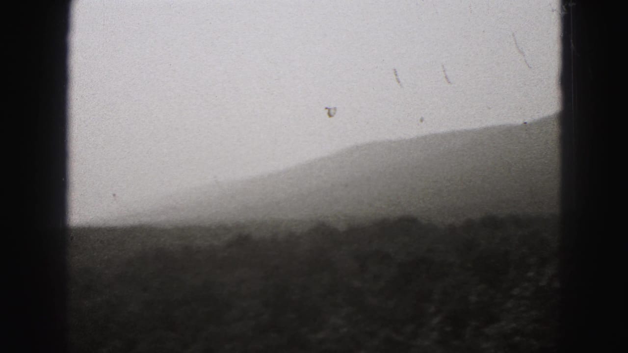 Soft 1946 8mm landscape frame showing layered Pennsylvania hills and dark foreground vegetation beneath a pale sky.