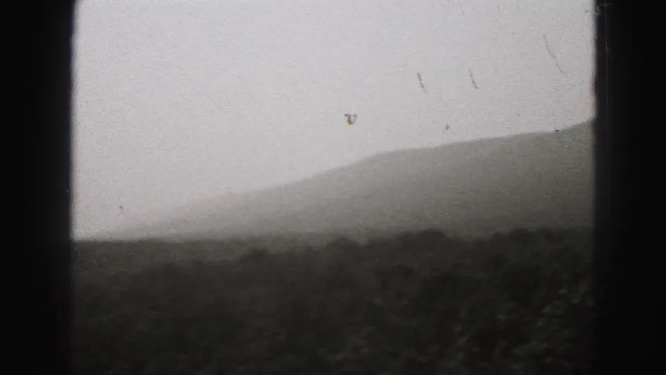 Soft 1946 8mm landscape frame showing layered Pennsylvania hills and dark foreground vegetation beneath a pale sky.