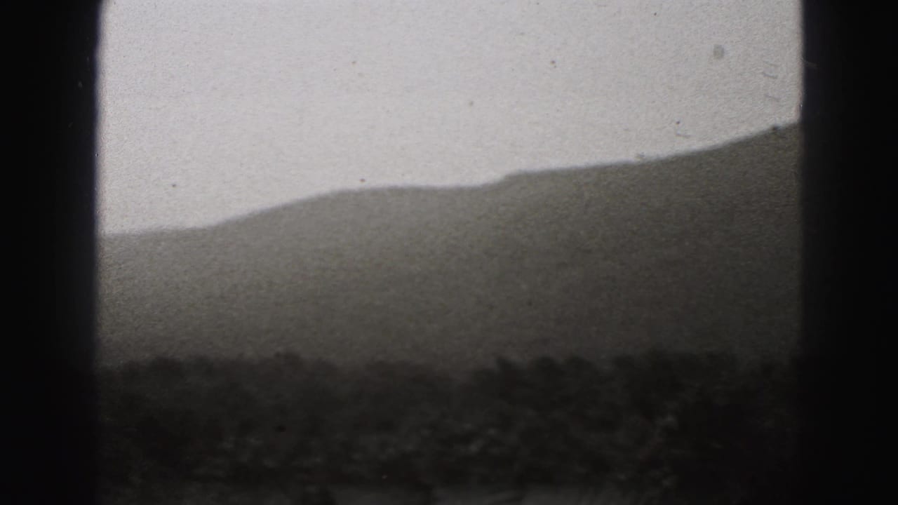 New Cumberland 8mm home-movie frame showing a dark wooded foreground and sloping hills fading into a pale overcast sky.