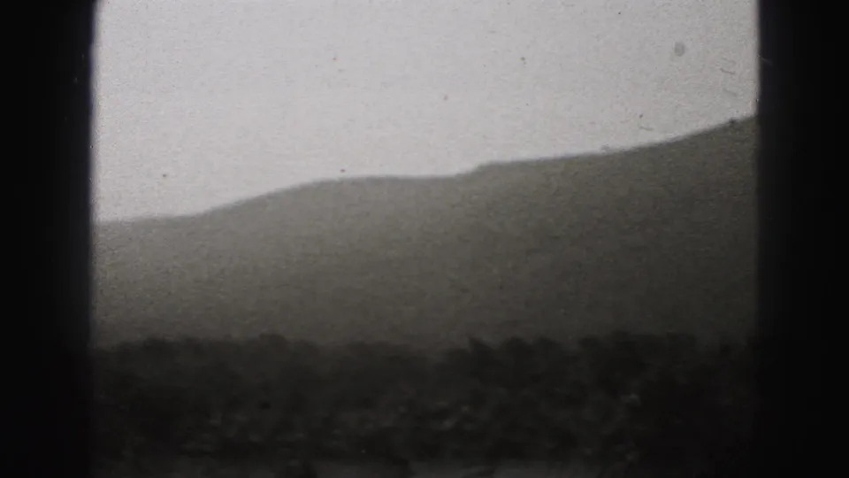 New Cumberland 8mm home-movie frame showing a dark wooded foreground and sloping hills fading into a pale overcast sky.