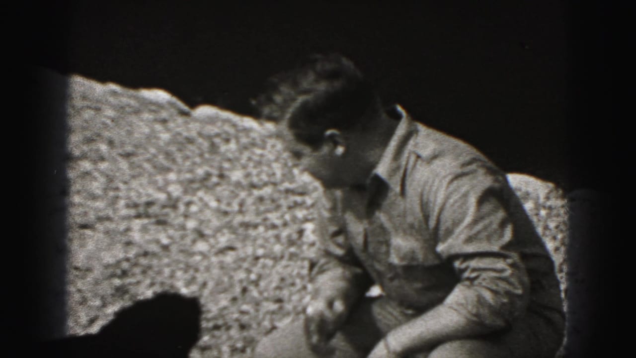 Man looks down beside the black puppy on gravel in a short 1946 home-movie scene from New Cumberland, Pennsylvania.