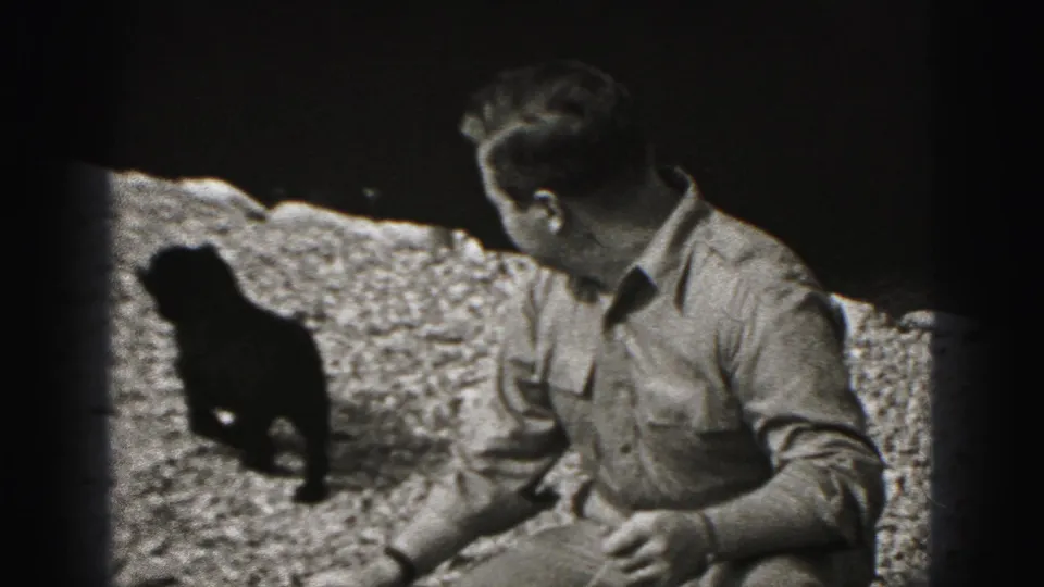 The man turns his head toward the small dark dog as it moves across the gravel in this 1946 Pennsylvania home-movie frame.