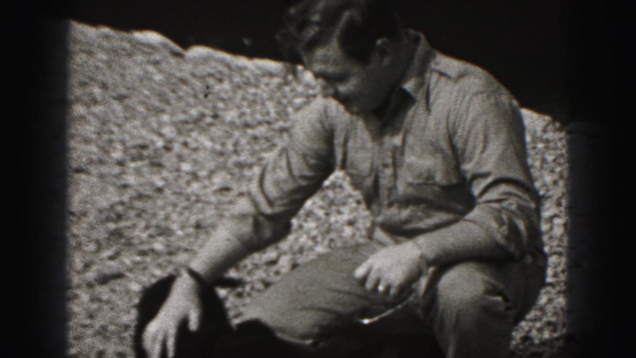 The man crouches and extends a hand toward the small dog in a 1946 New Cumberland outdoor home-movie frame.