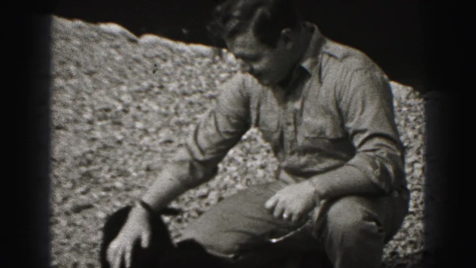 The man crouches and extends a hand toward the small dog in a 1946 New Cumberland outdoor home-movie frame.