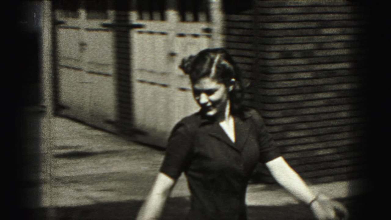 Woman in a dark dress walks outdoors near a brick building and wooden fence in New Cumberland, Pennsylvania.