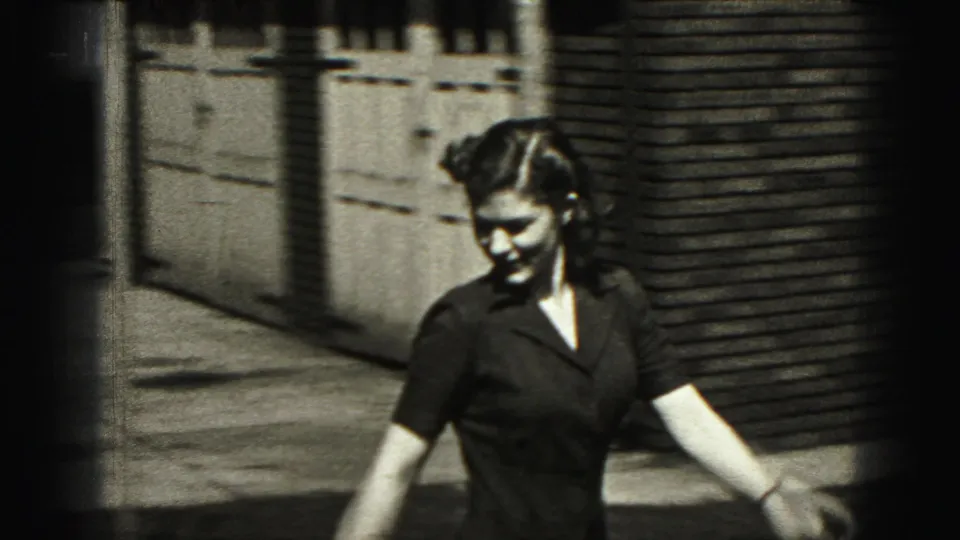 Woman in a dark dress walks outdoors near a brick building and wooden fence in New Cumberland, Pennsylvania.