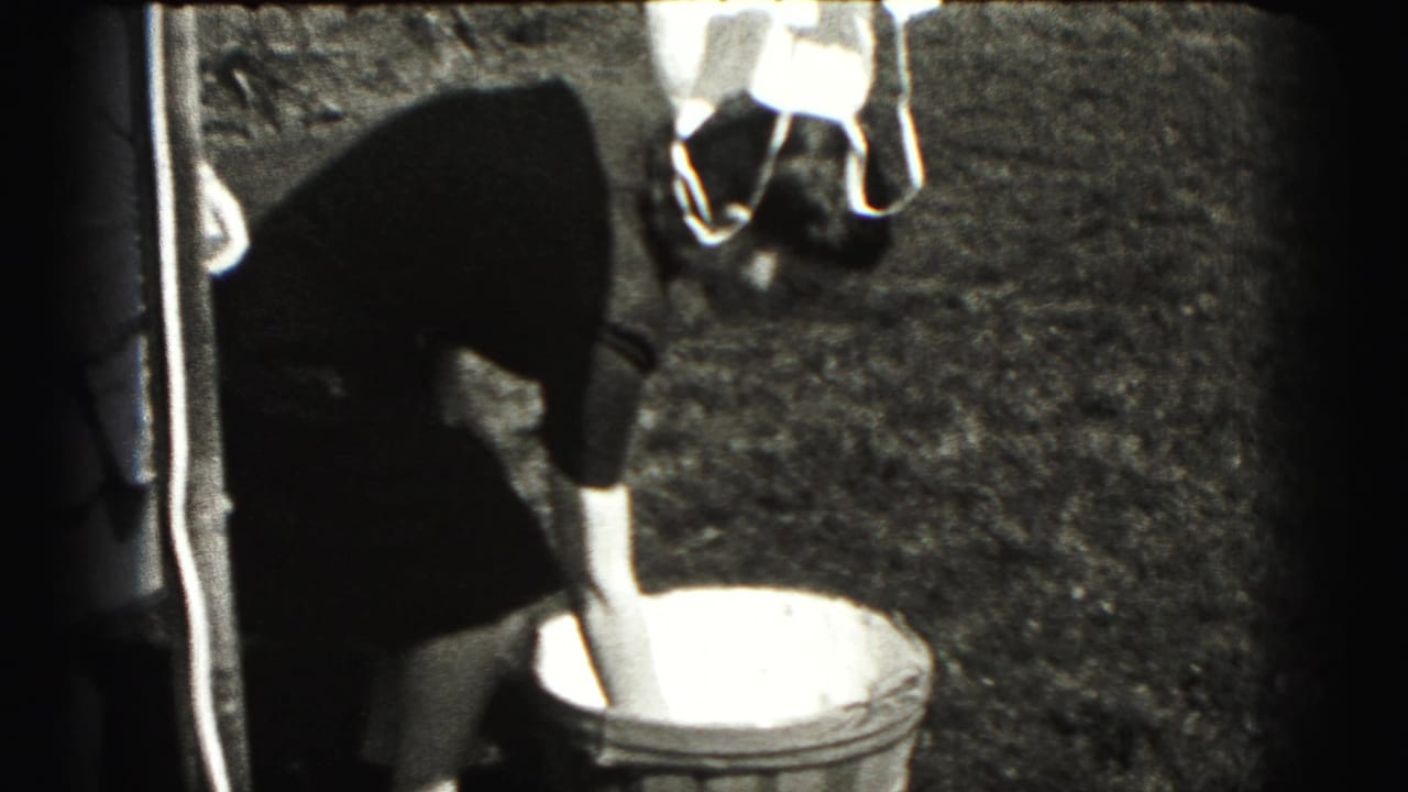 Woman in a dark dress bends toward a round tub in a grassy yard in 1940s home-movie footage.
