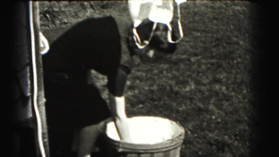 Woman in a dark dress bends toward a round tub in a grassy yard in 1940s home-movie footage.