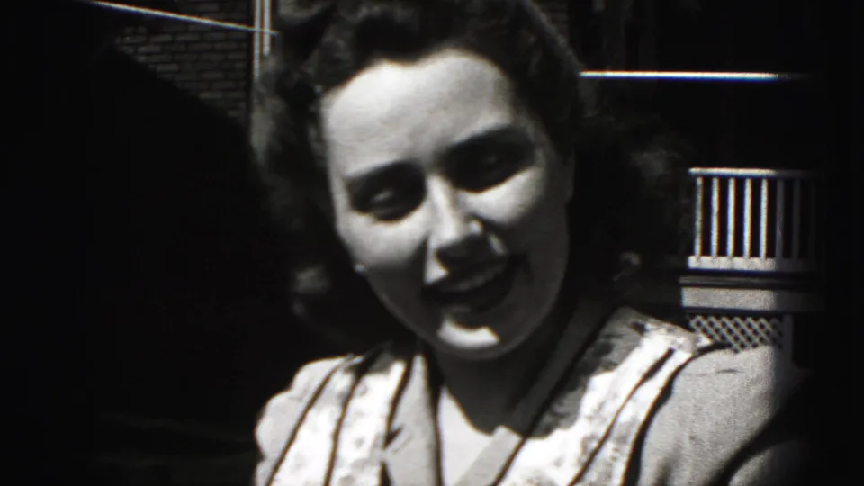 In the 1946 New Cumberland footage, the woman begins smiling toward the camera beside a railing and building exterior.