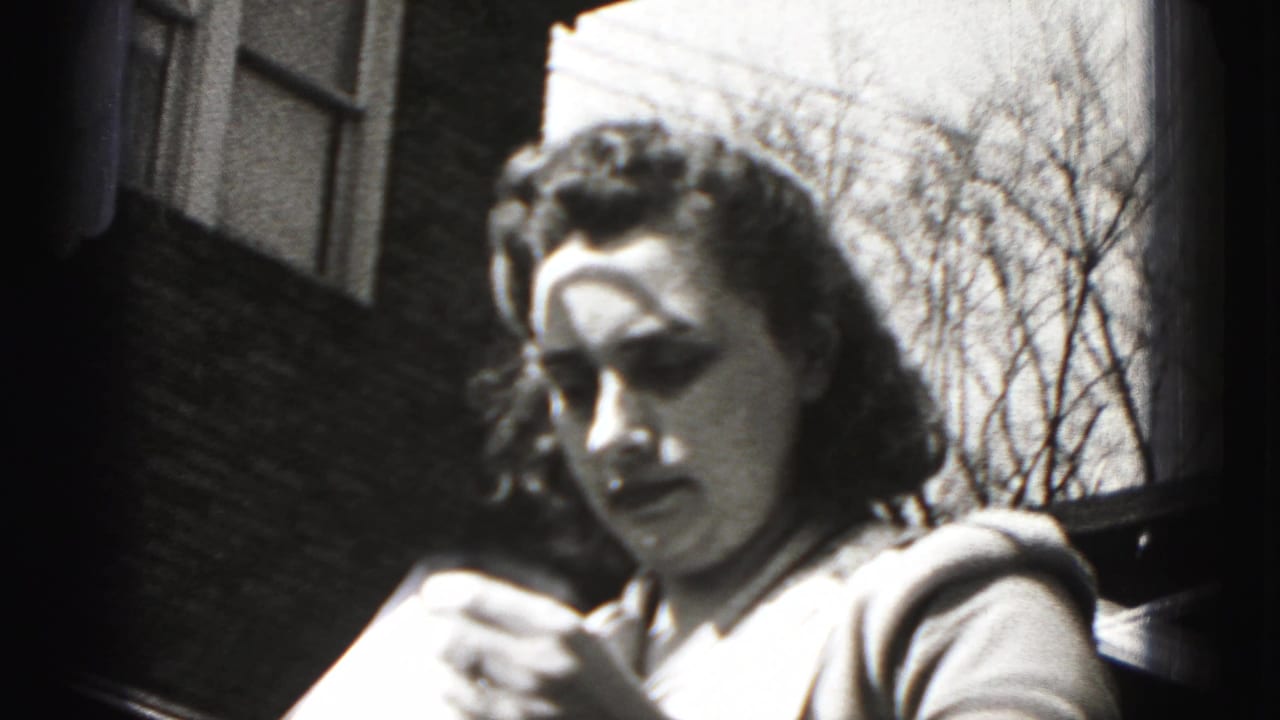 In 1946 New Cumberland, Pennsylvania, a woman in a patterned apron handles fabric near a brick building in bright sun.