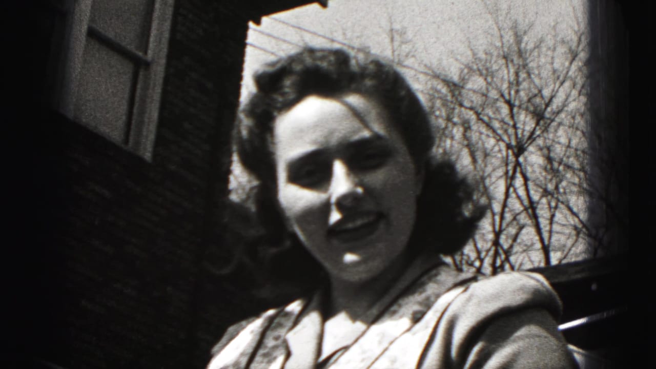 A woman in a patterned apron faces the camera during a 1946 outdoor home-movie moment in New Cumberland, Pennsylvania.