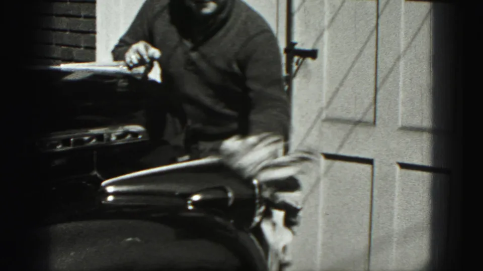 The man stands near the car's hood and front fender, holding a cloth in the bright 1946 outdoor scene.