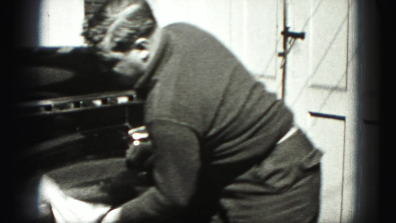 Man leaning over the front of a dark car with a cloth near a garage door.