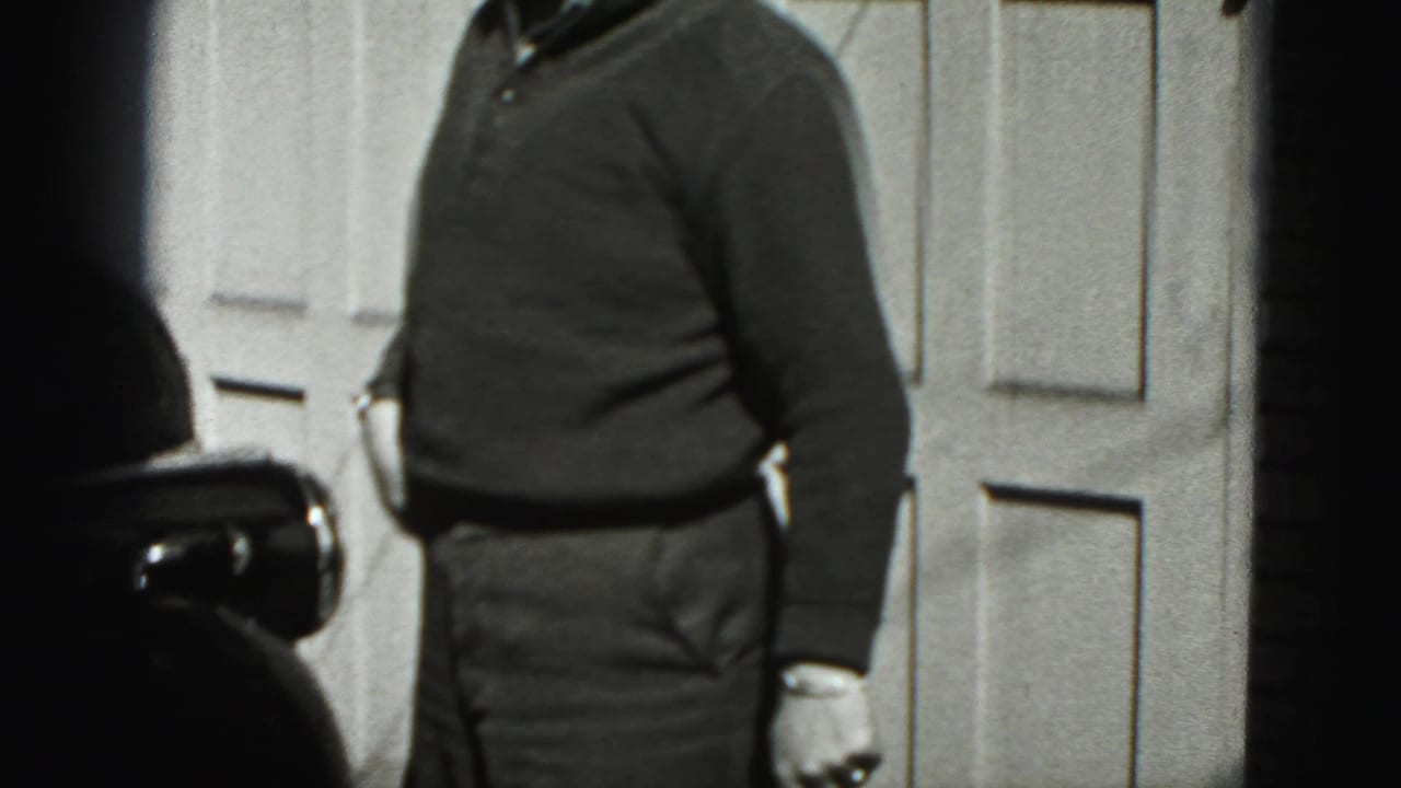 Partially framed man standing near a paneled garage door in sunlight.