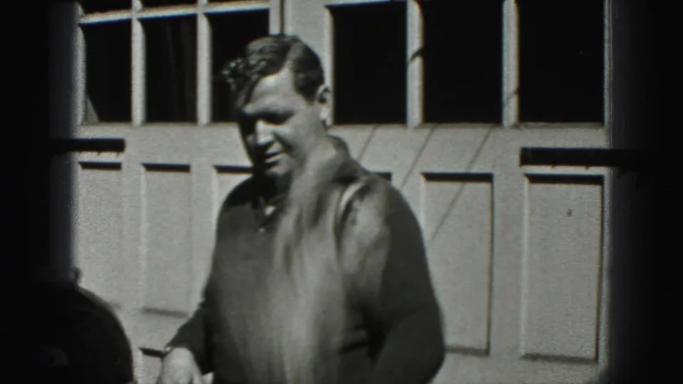 An adult man in a dark sweater stands outside a garage door in New Cumberland, Pennsylvania, in 1946 footage.