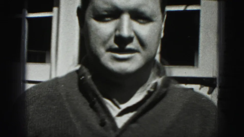 A close, slightly soft 8mm frame shows the man facing the camera outside a garage door in 1946 New Cumberland footage.