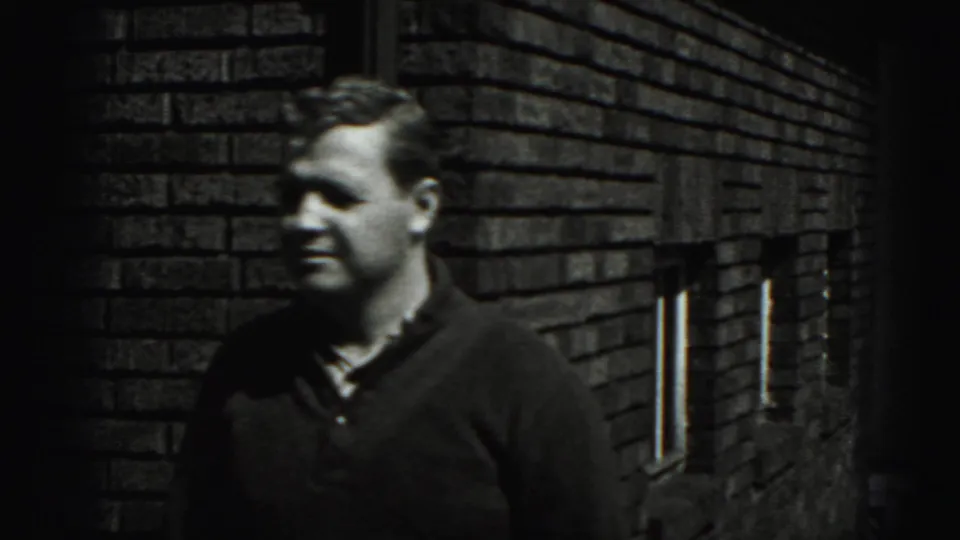 In the 1946 New Cumberland home-movie footage, an adult man stands by a brick wall and looks away from the camera.